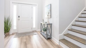 En gang med en hvid dør, et konsolbord med en lampe og en trappe.