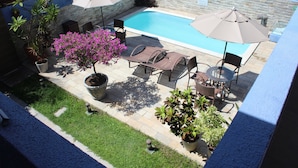 Un área de piscina en la azotea con sillones de descanso, sombrillas y plantas en macetas.