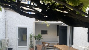 A covered patio area with a wooden table and chairs, potted plants, and a bench.