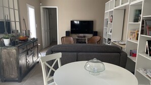 A living room with a sofa, a dining table with chairs, a TV, and a bookshelf.