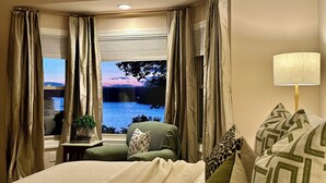 Una habitación de hotel con una cama, un escritorio con lámpara y vistas a un lago al atardecer.