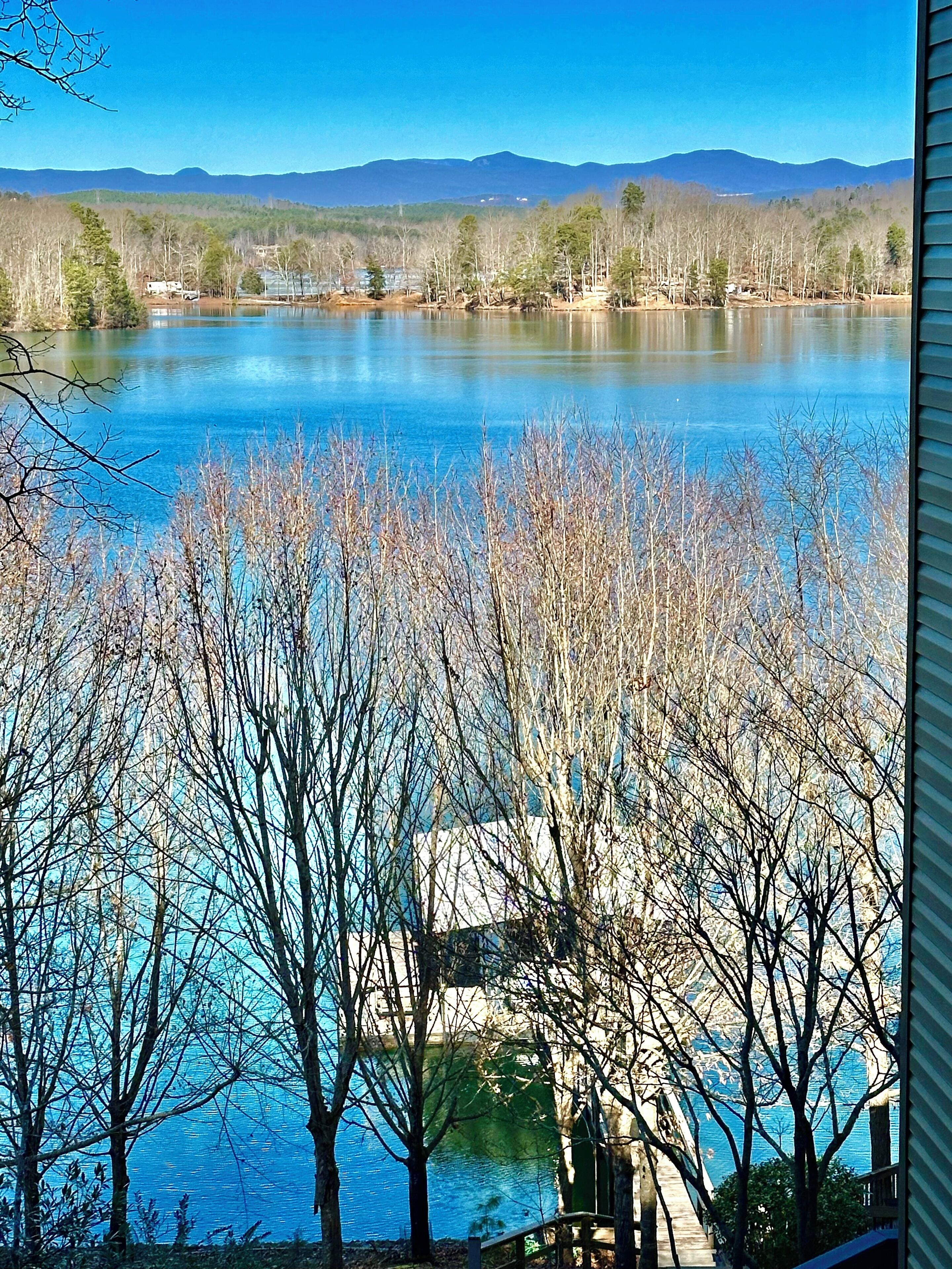 A view of a lake with mountains in the background, surrounded by trees and a house.