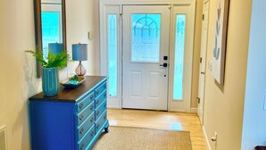 Un pasillo con un aparador azul, un espejo, una lámpara y una puerta con paneles de vidrio esmerilado.