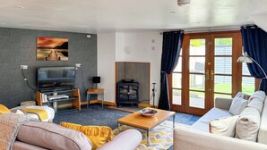 A living room with a sofa, a coffee table, a TV, a fireplace, and a large window. - 2 bedroom accommodation in Carterton (Carterton)