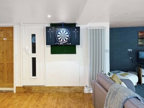 A room with a dartboard, a wooden door, a radiator, a sofa, and a television. - 2 bedroom accommodation in Carterton (Carterton)