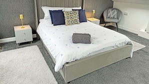 A bedroom with a sloped ceiling, a skylight, a bed with patterned bedding, two bedside tables with lamps, and a chair. - 2 bedroom accommodation in Carterton (Carterton)