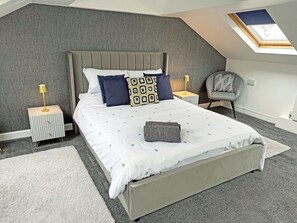 A bedroom with a sloped ceiling, a skylight, a bed with patterned bedding, two bedside tables with lamps, and a chair. - 2 bedroom accommodation in Carterton (Carterton)