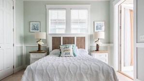 Quarto com cama, duas mesas de cabeceira, janela com persianas e uma porta.