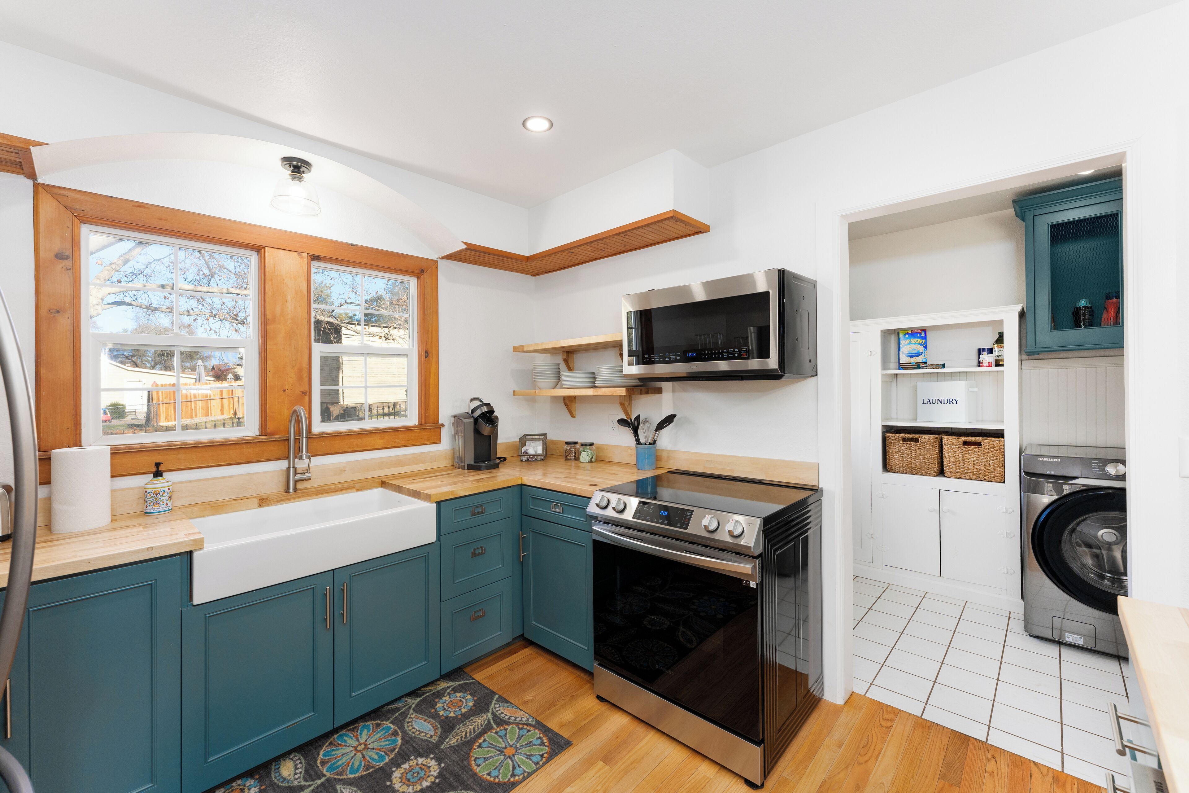 A modern kitchen with teal cabinets, a built-in oven, a microwave, and a washing machine.