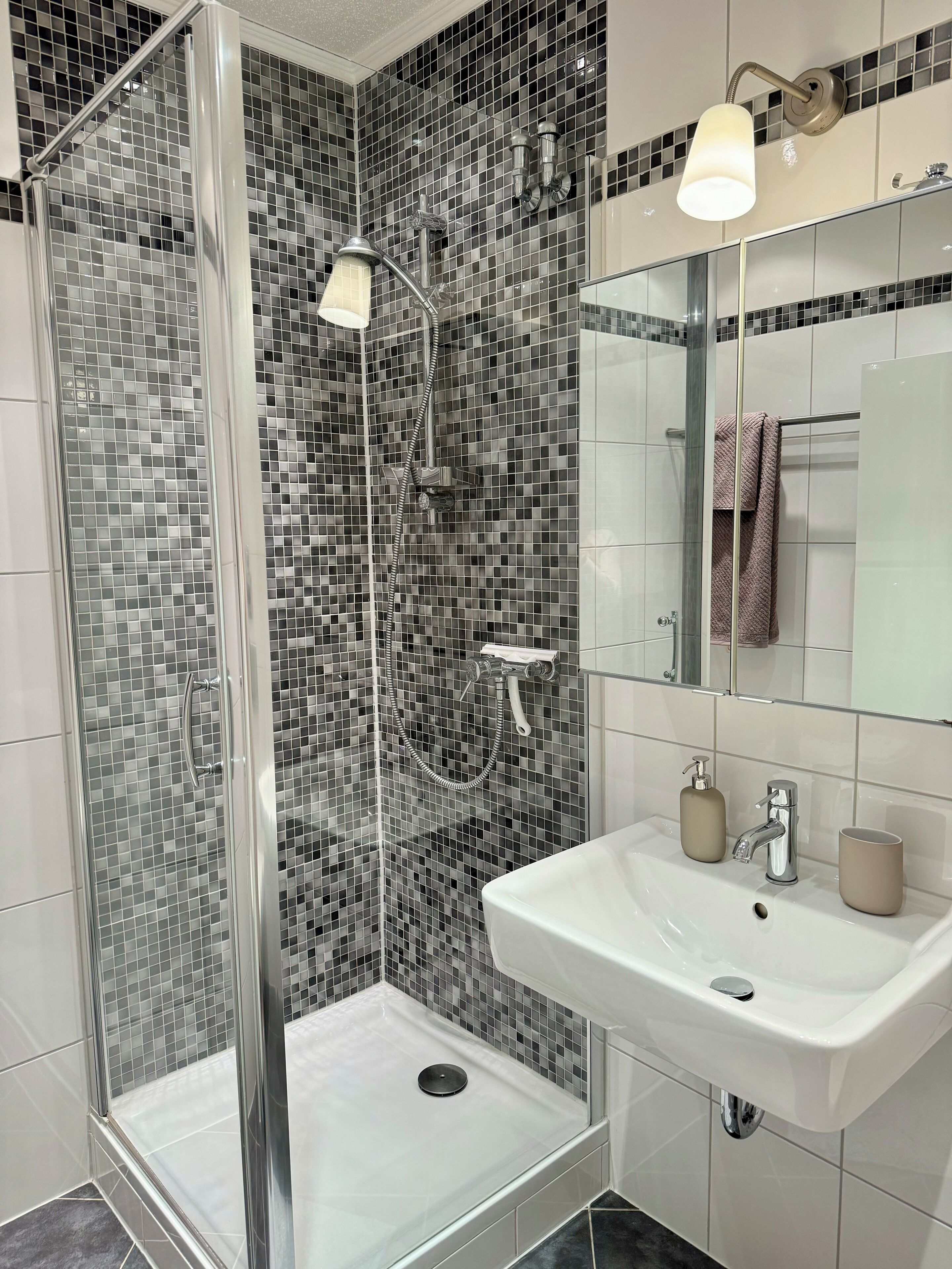 A modern bathroom with a glass-enclosed shower, a white sink, and a mirror above it.