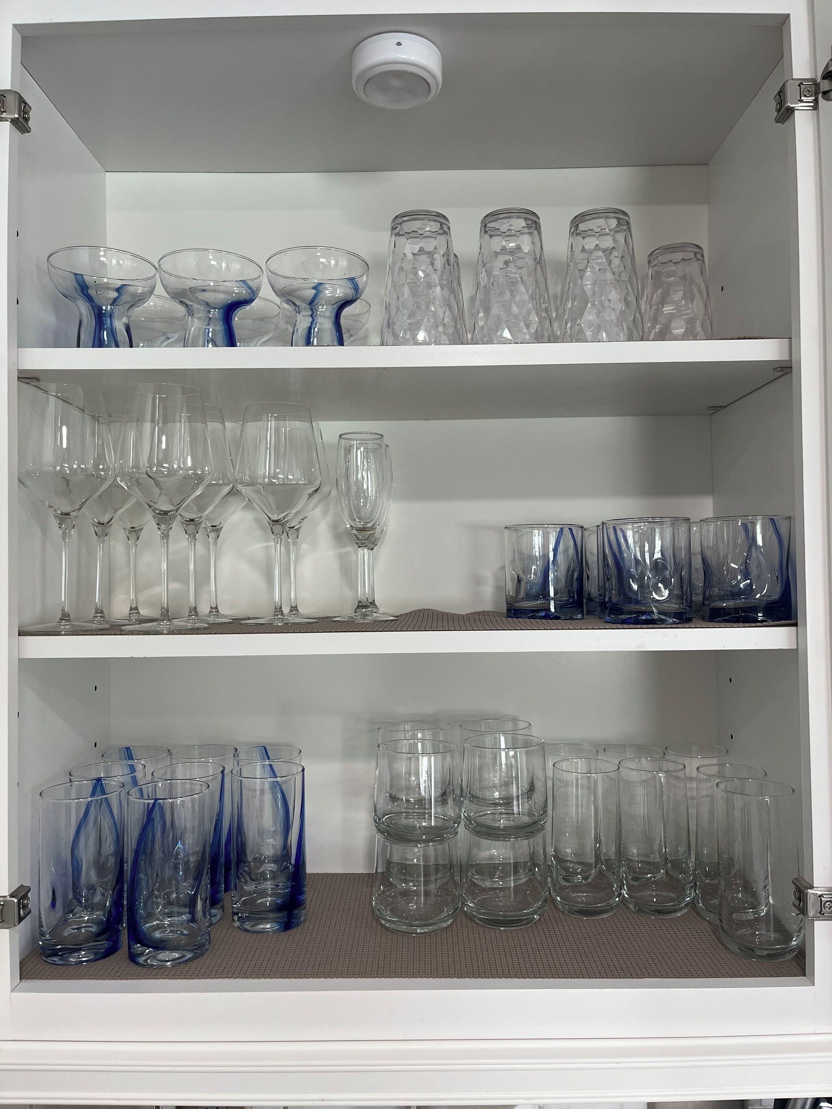 Un meuble avec des étagères contenant divers objets en verre, notamment des verres à vin, des verres à cocktail et des vases.