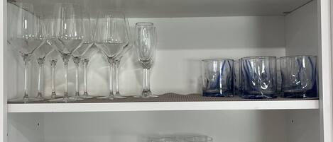 Un meuble avec des étagères contenant divers objets en verre, notamment des verres à vin, des verres à cocktail et des vases.