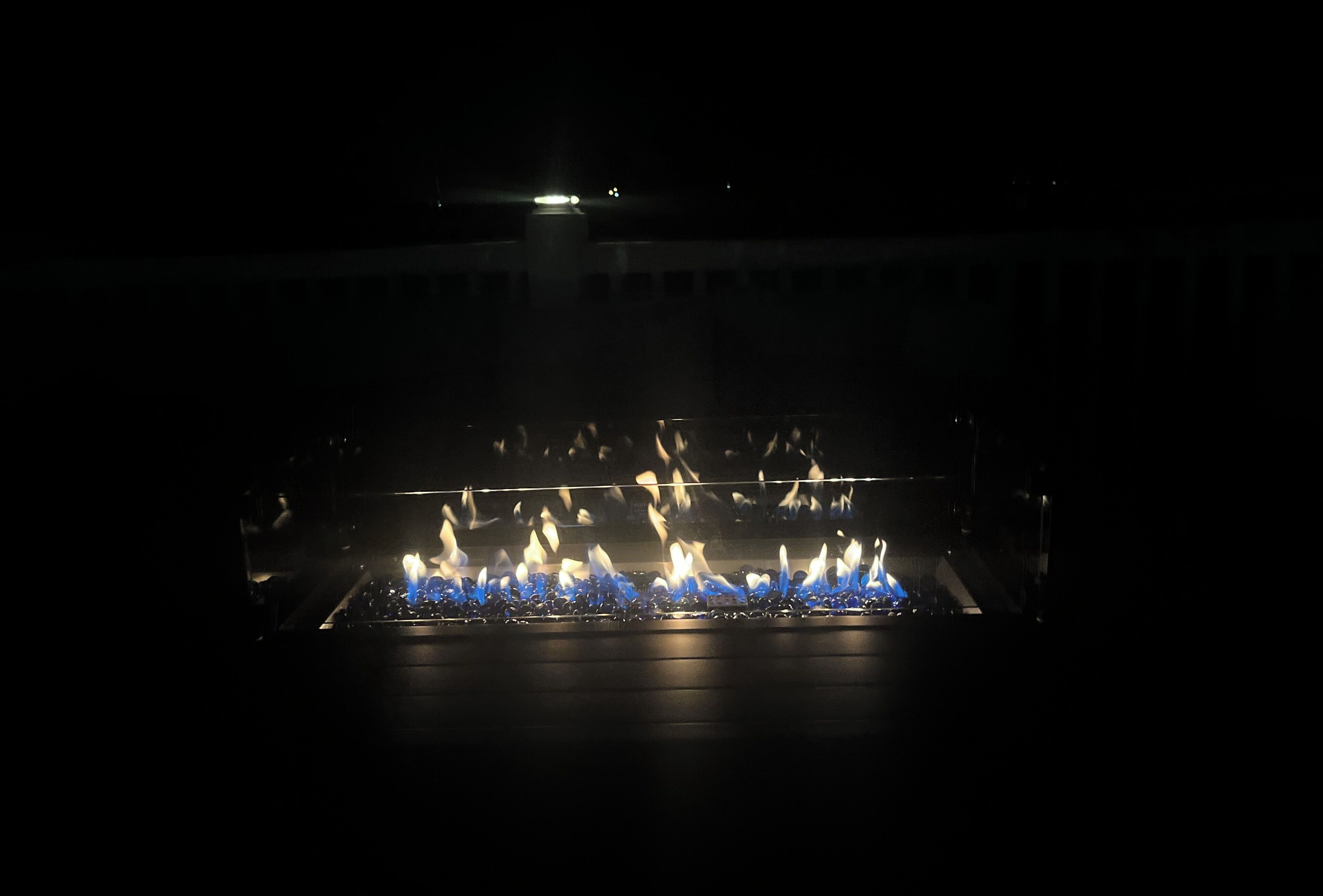 A gas fireplace with blue flames, set in a dark room with a visible ceiling and walls.