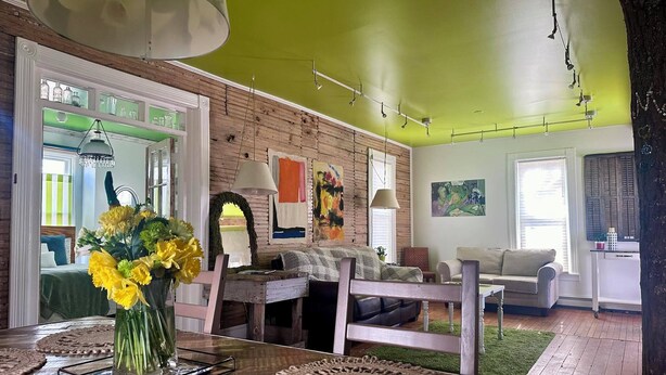 A living room with a wooden table, a vase of yellow flowers, a couch, and a dining table with placemats. - Cute & Artsy Condo 1mi from Crystal lake, & 7mi from Frankfort (Benzonia)