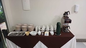 Montaje de bufé con platos, tazones, cubiertos y una máquina de café.