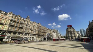 Una amplia plaza con edificios históricos, mesas al aire libre y un cielo azul despejado.