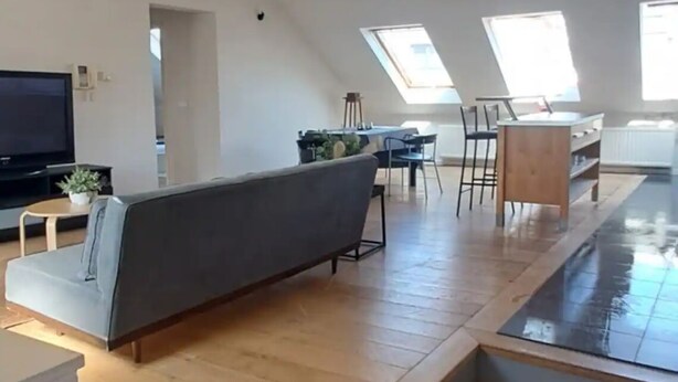 Una sala moderna con piso de madera, un sofá gris, un televisor y un comedor con sillas y una mesa.