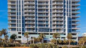 Un hôtel de grande hauteur doté de nombreux balcons, pr ésentant une architecture moderne et se dressant sur fond d’un ciel bleu azur.