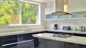 A modern kitchen with a large window, black cabinets, a gas stove, a coffee maker, a blender, and a microwave.
