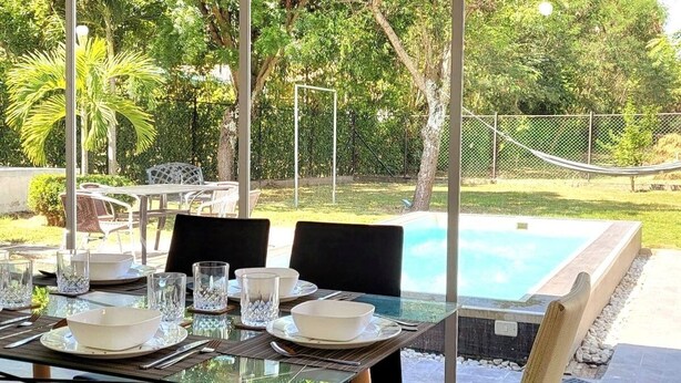 An outdoor dining area with a table set for four, overlooking a swimming pool and lush greenery.
