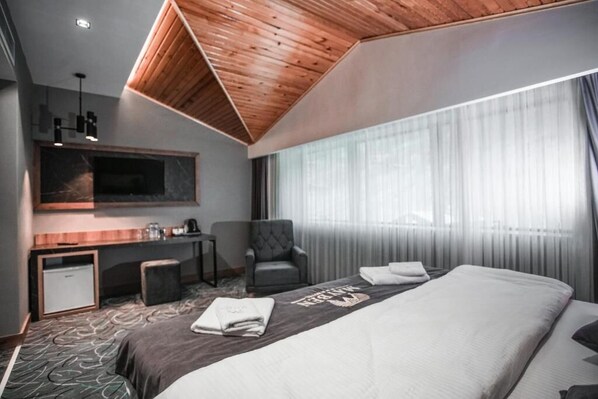 A modern hotel room with a large bed, a desk, a chair, and a TV mounted on the wall. - MAYBEN HOTEL (Çaykara)
