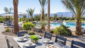 An outdoor dining area with a table set for four, surrounded by palm trees and a pool.