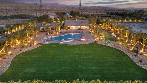 A residential property with a swimming pool, landscaped garden, and a view of the surrounding desert landscape.