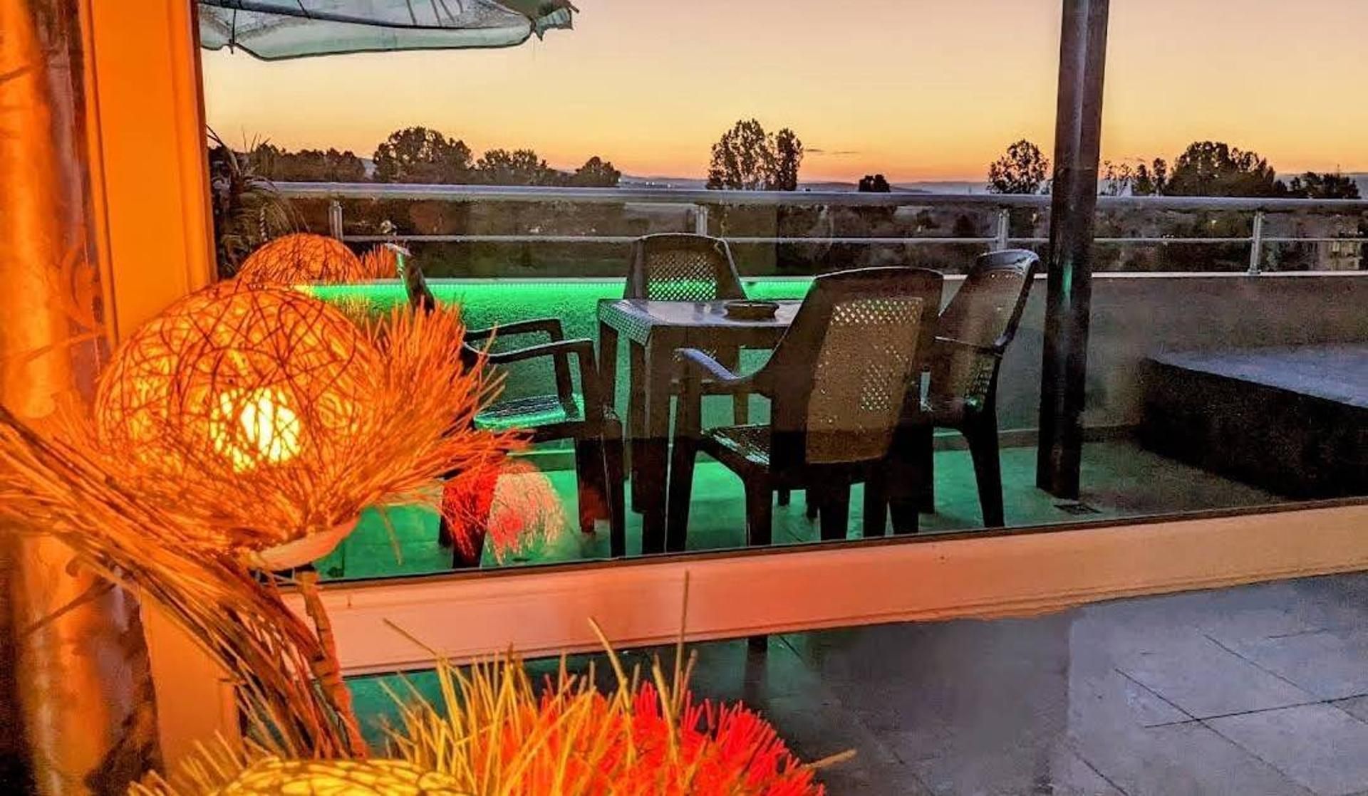 Ein Außenbereich mit Sitzgelegenheit, Tisch, Stühlen, einer Zierleuchte und Blick auf die Landschaft.