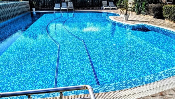 Una piscina con agua azul cristalina, un borde con baldosas y sillas de descanso.