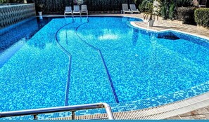 Una piscina con agua azul cristalina, un borde con baldosas y sillas de descanso.