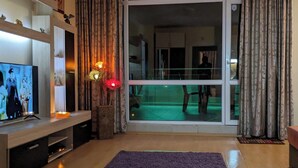 Un salón con una televisión de pantalla plana, una alfombra púrpura y un ventanal corredero que da a un balcón.
