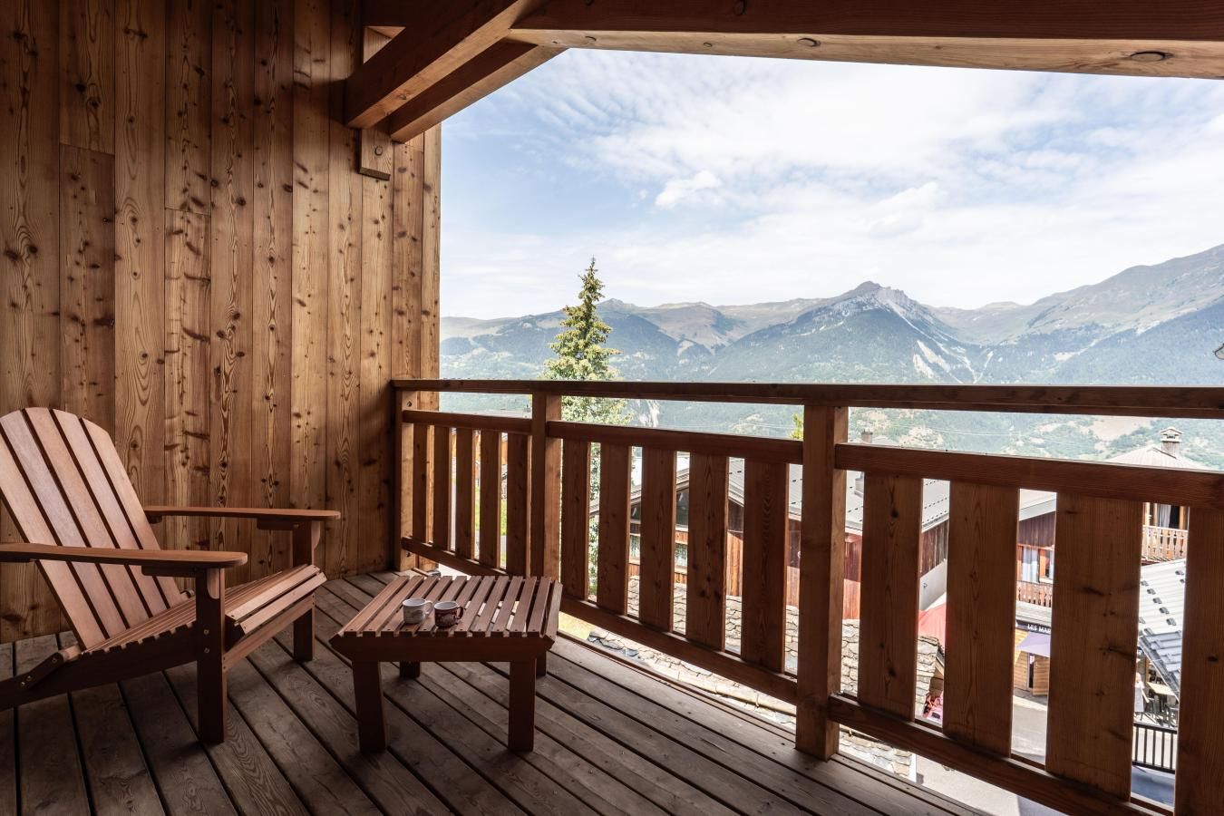 A wooden deck with a wooden chair and table, overlooking a mountainous landscape.
