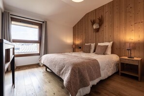 Ein Schlafzimmer mit einem Holz-Kopfteil, einem großen Bett mit weißer Bettwäsche, einem Nachttisch mit Lampe und einem Fenster mit Vorhängen.