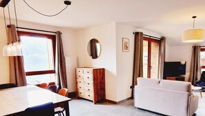 A modern living room with a dining area, a TV, and a wooden cabinet. - 50m from ski slopes, 1st floor, view resort, balcony, tv, 86m², Montalbert (La Plagne)