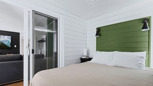 A bedroom with a sliding door, a bed with white pillows, a green headboard, and a wall-mounted lamp. - Earthy Pearl - 1 Bedroom Suite @ the Boise Depot (Boise)