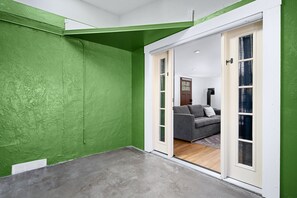 Een kamer met groene wanden, een grijze bank en een schuifglazen deur naar een andere ruimte.