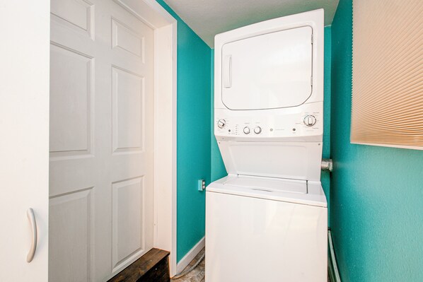 A laundry room with a white washer and dryer, teal walls, and a white door.