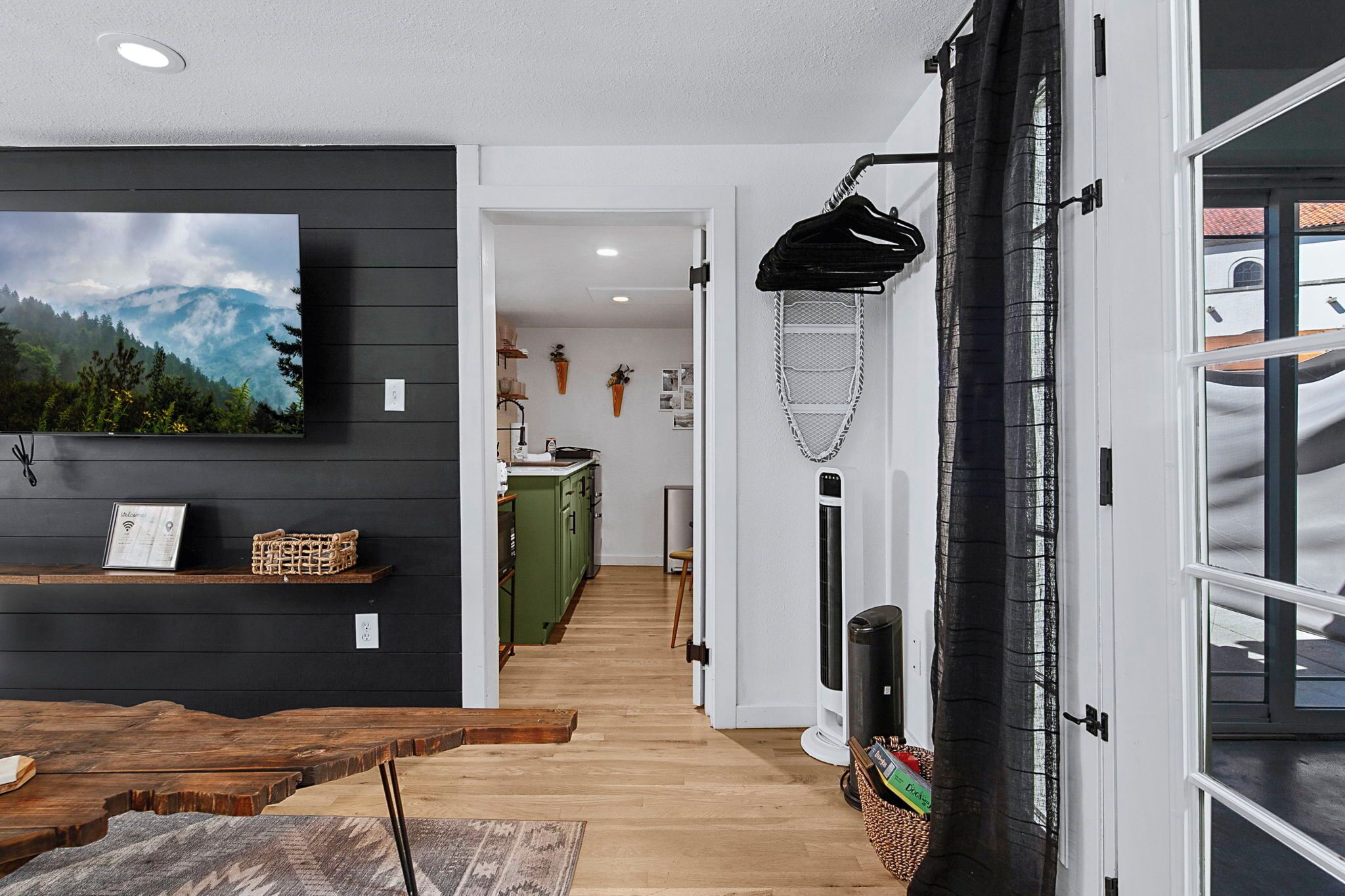 Un interior moderno con suelo de madera, televisor montado y cortina negra.