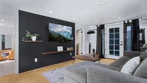 A modern living room with a flat-screen TV, wooden shelves, a grey sofa, and a wooden coffee table. - Earthy Pearl - 1 Bedroom Suite @ the Boise Depot (Boise)