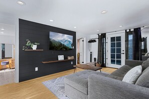 Ein modernes Wohnzimmer mit Flachbildfernseher, Holzregalen, einem grauen Sofa und einem Holztisch.
