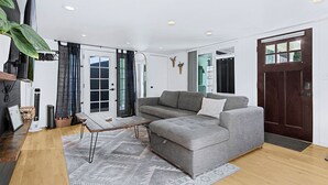 A modern living room with a grey sectional sofa, a small wooden coffee table, a large plant, and a sliding glass door leading to a balcony. - Earthy Pearl - 1 Bedroom Suite @ the Boise Depot (Boise)