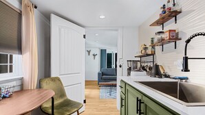 A compact kitchen with a sink, countertop, and green cabinets. There is a dining area with a table and a chair. - Earthy Pearl - 1 Bedroom Suite @ the Boise Depot (Boise)