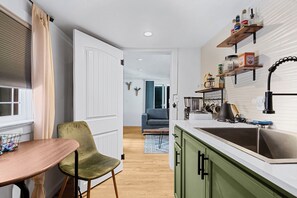 Una cocina compacta con un lavamanos, encimera y armarios verdes. Hay un comedor con una mesa y una silla.