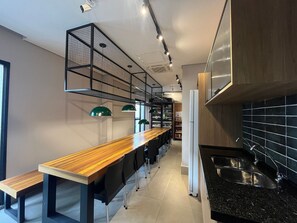 A modern kitchen with a black countertop, stainless steel sink, and a wooden dining table with chairs. - Studio no coração de perdizes (São Paulo)