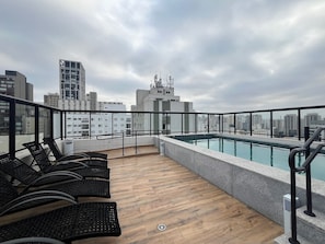 A rooftop pool area with lounge chairs, a pool, and a cityscape view. - Studio no coração de perdizes (São Paulo)