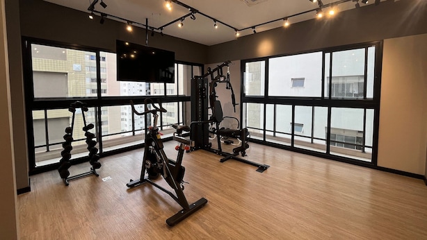 Une salle de sport dotée de grandes fenêtres, d’appareils d’exercice et d’un téléviseur fixé au plafond.