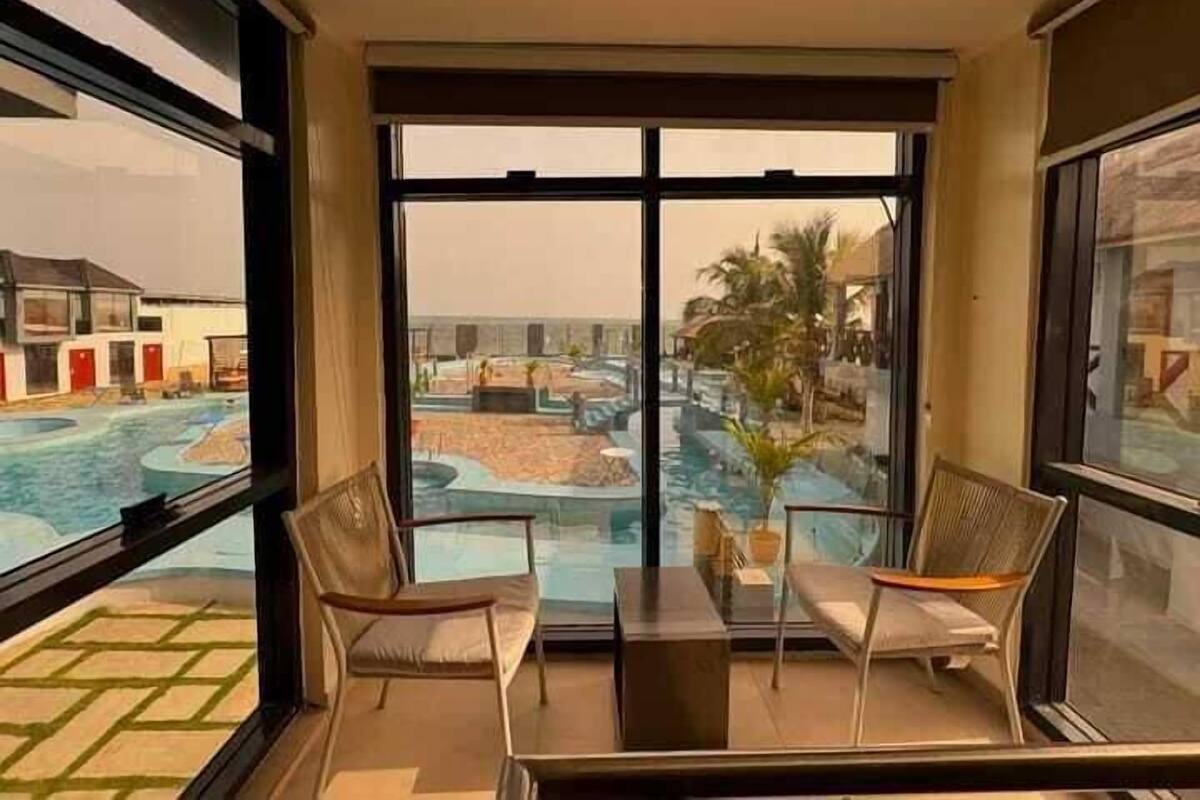 Ein Zimmer mit großem Fenster und Blick auf einen Poolbereich, zwei Stühle und ein kleiner Tisch.