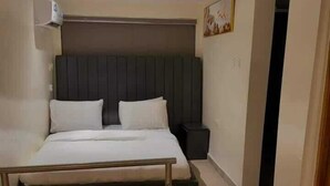 Een opgemaakt bed met hoofdeinde, nachtkastje en een kleine prullenbak.