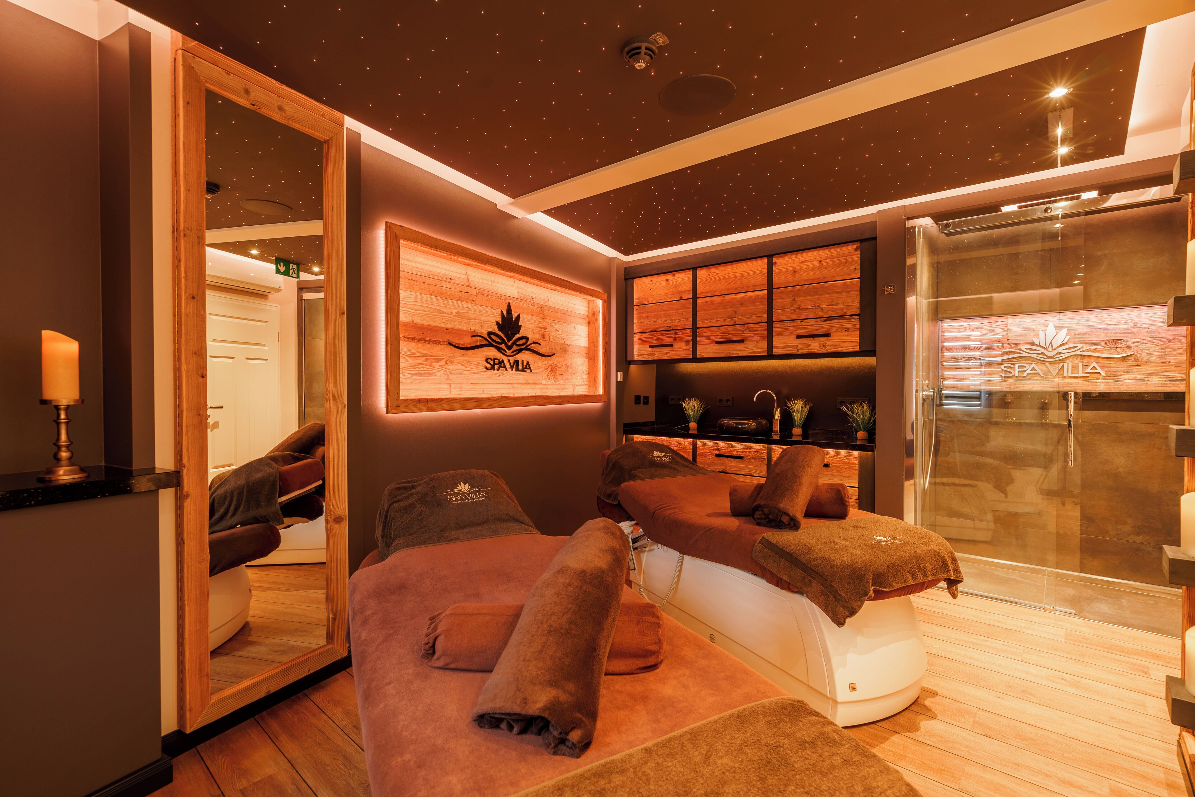 Een spa ruimte met een massagetafel, houten planken en een douchecabine van glas.