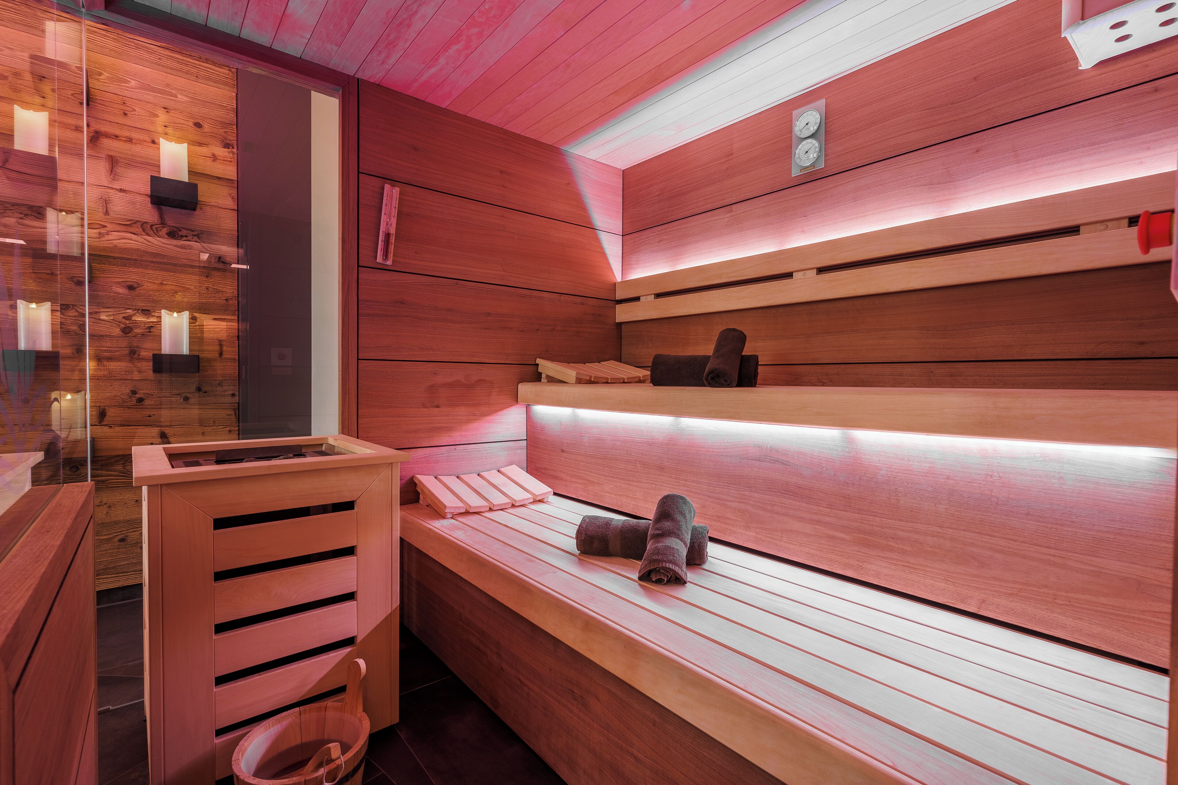 A sauna with wooden benches, a wooden wall, and a glass partition.